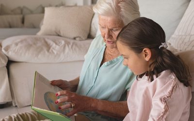 Side view of a grandmother and granddaughter reading story book in living room at home